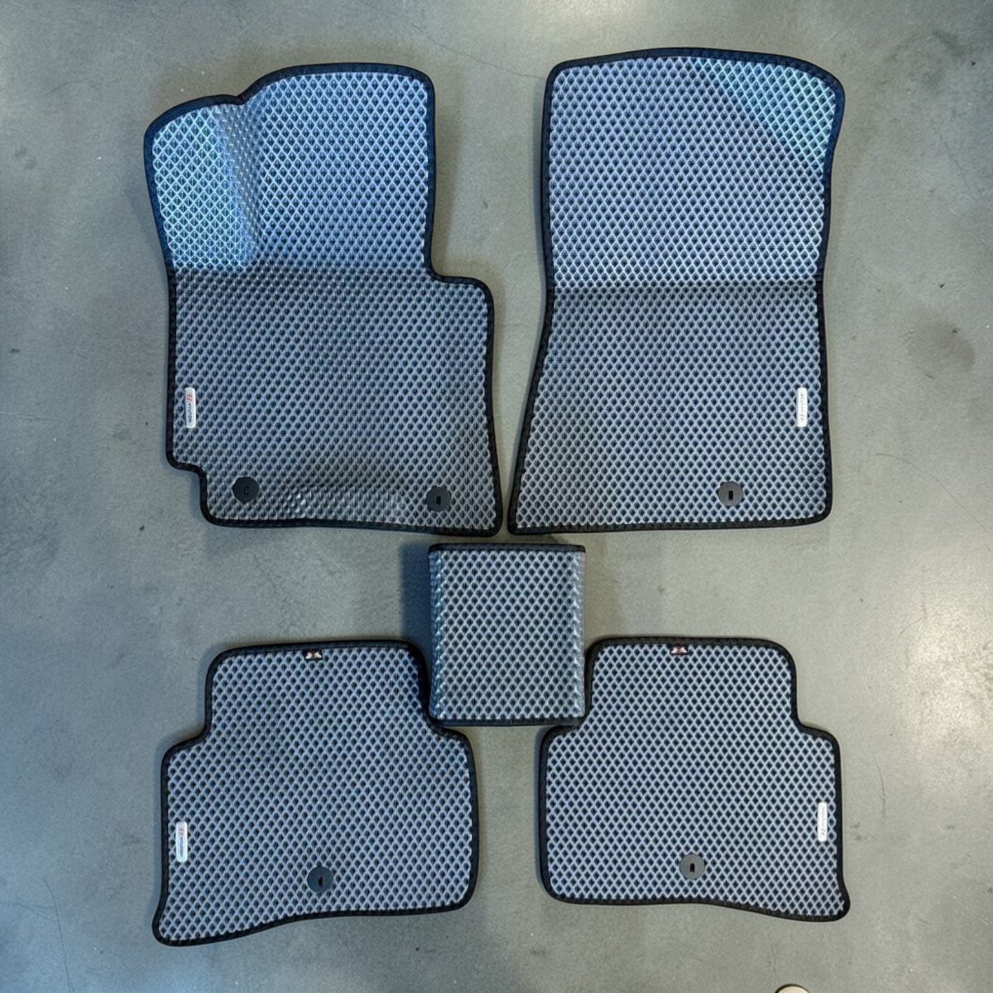 Set of car floor mats with a honeycomb pattern on a concrete floor.
