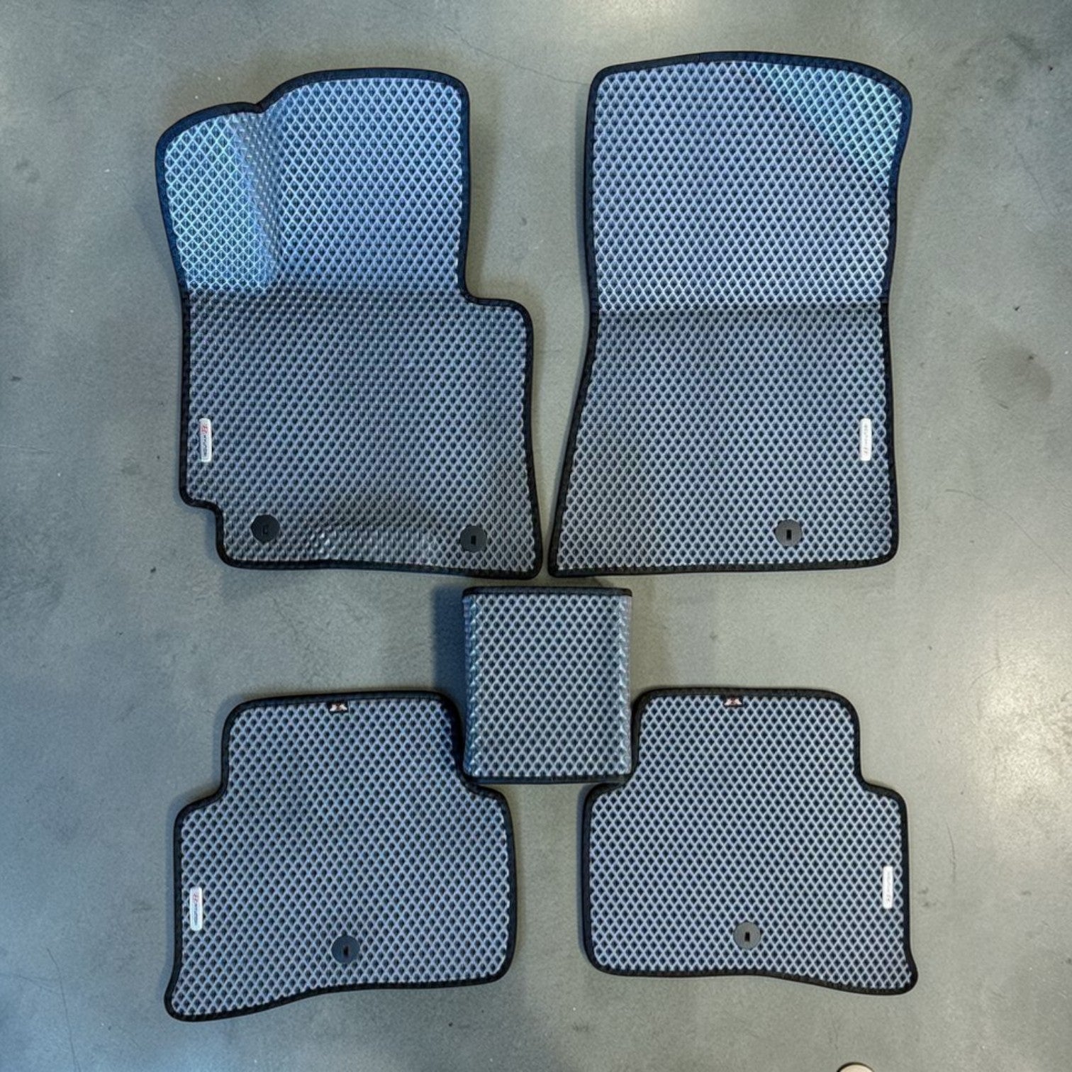 Set of car floor mats with a honeycomb pattern on a concrete floor.