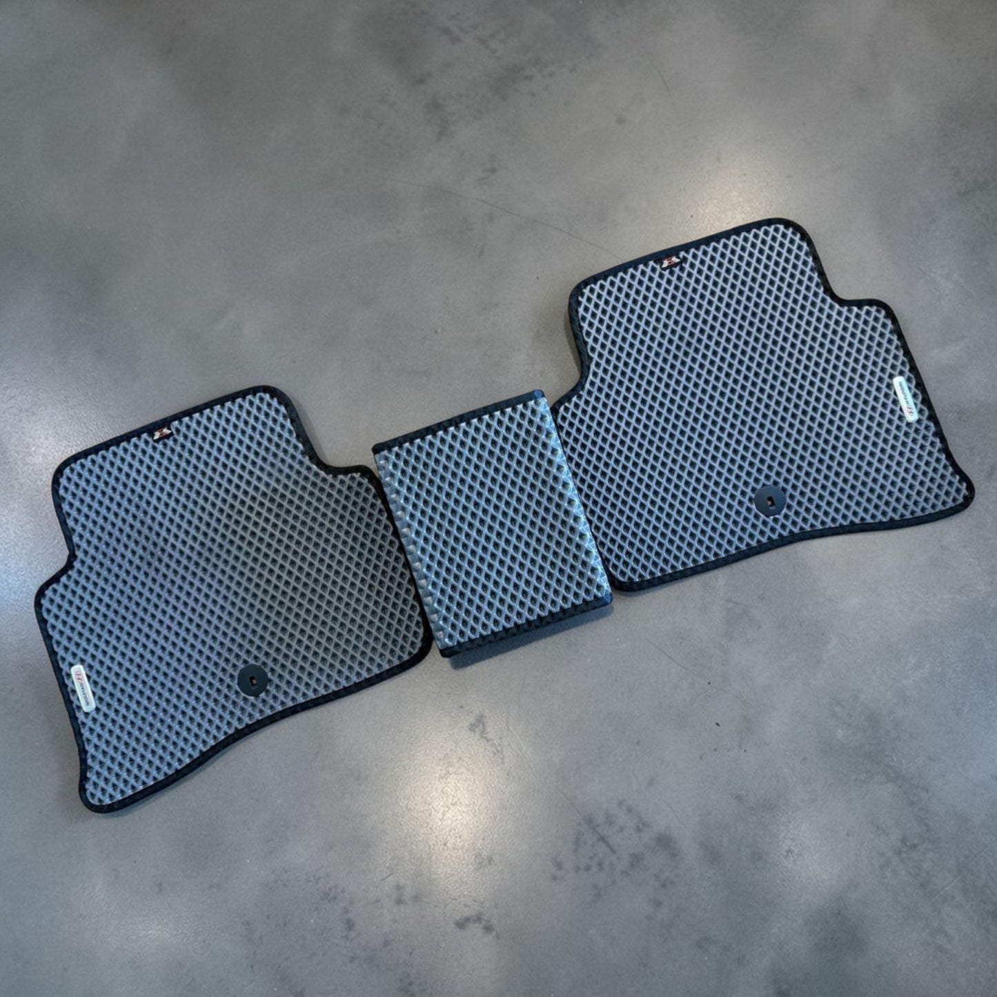 Three car floor mats with a textured pattern on a concrete floor.